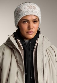 Pletená čelenka vyrobená z mäkkého vlákna, s jemnou krémovou a béžovou farbou a jemným vzorom snehových vločiek, poskytujúca teplo a pohodlie.