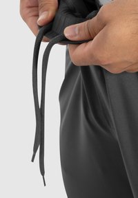 Graue Hose mit einem Kordelzugbund. Eine Hand hält den Kordelzug, der strukturiert und rund ist. Der Stoff sieht glatt und leicht aus.