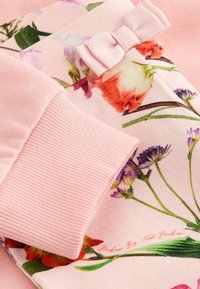 Tela de estampado floral rosa con puños acanalados; presenta un pequeño lazo a juego. Texto visible en la parte inferior que dice "Diseñado por Ted Parker."