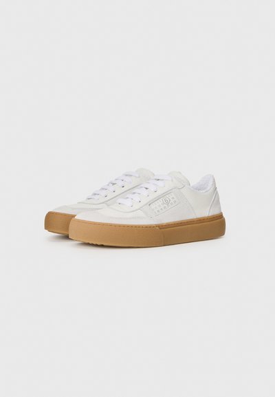 Vita canvas sneakers med en texturerad yta, med gummisulor, platta snören och en sidomärkning med numeriska detaljer.