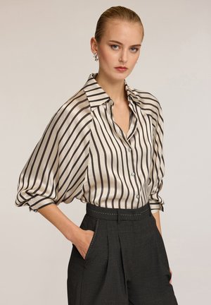 Blusa di seta con strisce verticali nere su fondo crema, dotata di colletto, chiusura frontale con bottoni e maniche ampie e arricciate.
