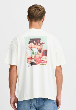White short-sleeve t-shirt featuring a colorful printed design on the back, depicting a table setting with drinks and people.