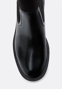 Czarne skórzane botki sięgające kostki o gładkiej fakturze, z elastycznymi panelami bocznymi i okrągłym noskiem. Smukła gumowa podeszwę akcentuje dolną część.
