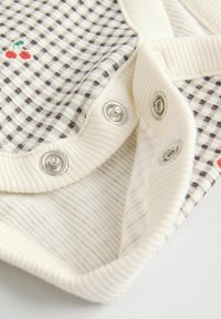 Medvilninė kūdikių kelnaitė su kreminiu fonu, dekoruota tamsiais languotais raštais ir siuvinėtų raudonųjų vyšnių motyvu. Užsegimai yra sidabrinės spalvos. Raišteliai su grioveliais.