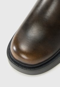 Brune lærstøvle tå med sort tyk sål, som viser en glat tekstur og en let slidt finish på en hvid baggrund.