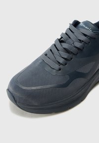 Scarpa sportiva grigia con tomaia in mesh, suola in gomma e dettagli testurizzati, con lacci rotondi e punta liscia.