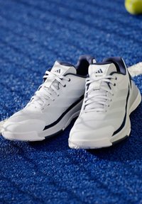 Bílé sportovní boty s texturovaným svrškem, námořnickými akcenty a polstrovanou podešví. Šňůrky jsou výrazné a design obsahuje tři pruhy.