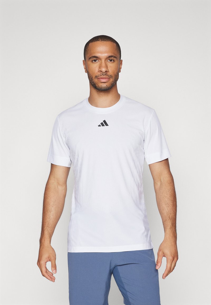 Bela atletska majica s kratkimi rokavi, narejena iz lahkotnega materiala, z okroglim izrezom in črnim Adidasovim logotipom na prsih.