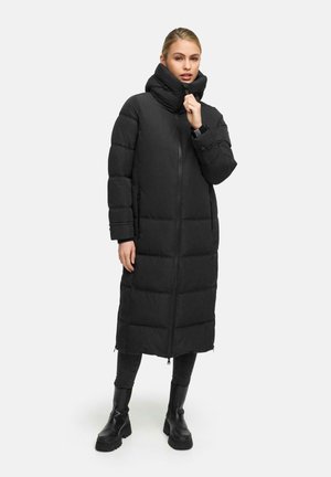 Cappotto lungo nero imbottito con colletto alto, chiusura a zip e texture trapuntata. Abbinato a jeans neri aderenti e stivaletti grossi.