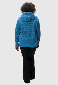 Haut de survêtement bleu à motifs, avec une capuche à cordon de serrage, des poignets et un ourlet côtelés. La texture est douce et il a une silhouette ajustée à la taille.