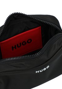 Sacchetto di stoffa nera con zip, contenente un portacarte rosso all'interno. Il portacarte mostra il nome del marchio "HUGO" in lettere nere.
