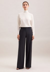 Biała bluzka z golfem i długimi rękawami zestawiona z czarnymi spodniami o wysokim stanie i szerokich nogawkach, charakteryzującymi się gładką teksturą i czystymi liniami.