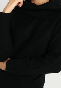 Schwarzer, übergroßer Pullover aus weichem Material, mit einem hohen, strukturierten Rollkragen und langen Ärmeln mit Rippbündchen.
