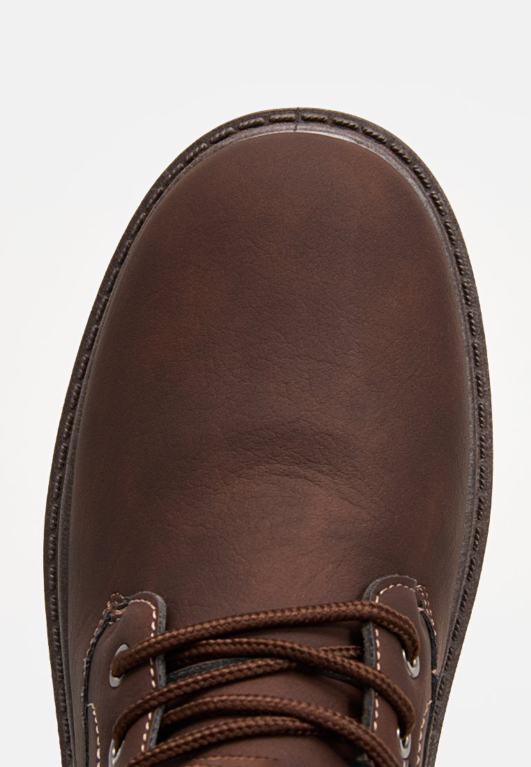 Scarpa di pelle marrone con punta tonda, cuciture in contrasto e lacci marroni. La suola presenta una finitura testurizzata per garantire aderenza.