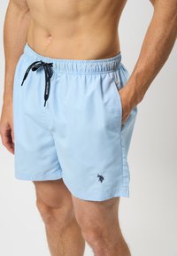 Lichtblauwe zwembroek van soepel stof, met een elastische tailleband en een trekkoord, en een klein geborduurd logo op het been.