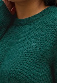 Zielony sweter dzianinowy o teksturowanym wzorze i ściągaczu przy dekolcie, charakteryzujący się średnią grubością i miękkim wyglądem.