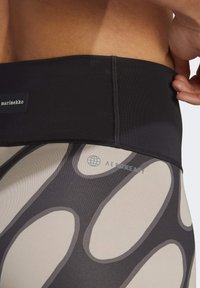 Leggings deportivos de cintura alta con una banda en negro, decorados con formas en gris y beige, etiquetados con "marimekko" y "AEROREADY."