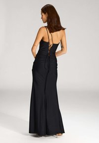 Robe noire longue jusqu'au sol avec des fines bretelles, des détails froncés à l'arrière et des accents à lacets. Tissu lisse et silhouette ajustée.