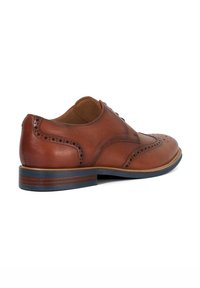 Brown leather dress shoe featuring brogue detailing, a rounded toe, and a contrast beige stitching. The heel has a blue accent layer.
