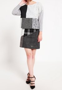 Patchwork-Kleid mit einer Mischung aus schwarzen, weißen und grauen Stoffen, die Texturen wie Spitze und Hahnentritt aufweisen, kurzen Ärmeln und geradem Schnitt.