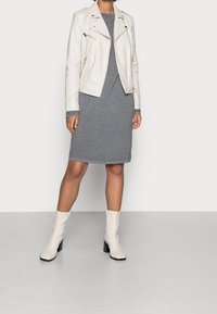 Giubbotto da motociclista in pelle bianca, abito a righe grigie e stivaletti bianchi con tacco. L'outfit presenta una combinazione di texture e linee eleganti.