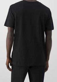 Musta puuvillainen t-paita lyhyillä hihoilla, rento malli ja pyöreä kaula-aukko; sileä pinta ilman näkyviä kuvioita tai koristeita.