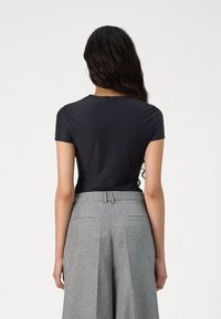 Black short-sleeve top with a round neckline paired with high-waisted, pleated gray trousers. Smooth fabric with a fitted shape.