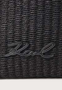 Black woven bag made of textured material, featuring a prominent, stitched "Karl" logo in contrasting white outline.