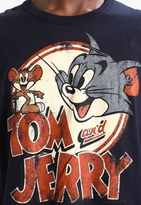 Un primer plano de una camiseta negra con personajes de dibujos animados, Tom y Jerry, sonriendo y juguetones, con el título "TOM y JERRY" destacado de forma prominente.