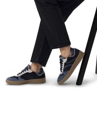 Sneaker in suede blu and navy con un accento in pelle bianca, suola in gomma testurizzata e dettagli cuciti, abbinate a pantaloni scuri.