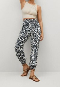 Pantalons amples à motif bleu marine et blanc, avec une taille élastique et des chevilles resserrées, associés à un haut sans manches beige.