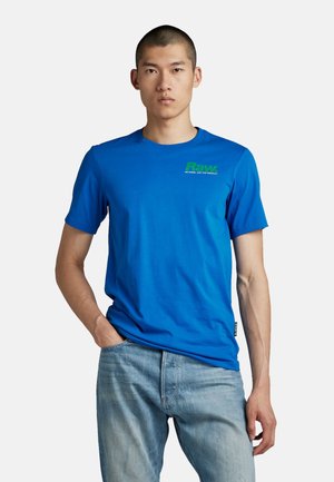 Blaues Baumwoll-T-Shirt mit kurzen Ärmeln und Rundhalsausschnitt, mit einem grünen Grafiklogo auf der linken Brust. Glatte Textur.