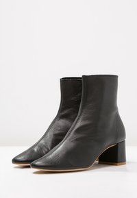 Botas de cuero negras hasta el tobillo con punta afilada y un tacón cuadrado grueso. Presentan una textura suave y un diseño minimalista.