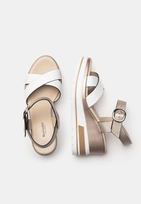 White and gold platform sandals with crisscross straps, a thick sole, and an adjustable ankle strap for support and stability.