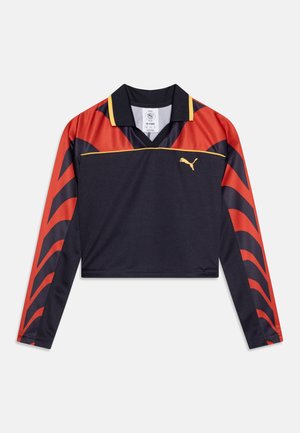 Skraćeni dugodrugi polo u tamnoplavoj boji s crvenim i crnim prugama. Ima klasičan ovratnik i žute detalje. Izrađen je od prozračnog materijala.