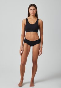 Schwarzer Sport-BH und passende Unterwäsche mit glatter Textur. Der BH hat breite Träger und ein Band mit der Aufschrift "SNOCKS". Einfaches, figurbetontes Design.