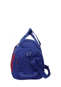 Sac de sport bleu avec des accents rouges, comportant un compartiment zippé, une sangle d'épaule réglable et des poignées de transport.