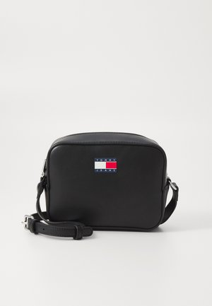 Bolso de hombro de cuero negro con forma rectangular, que presenta un parche de logo frontal en rojo, blanco y azul. Incluye correa ajustable.