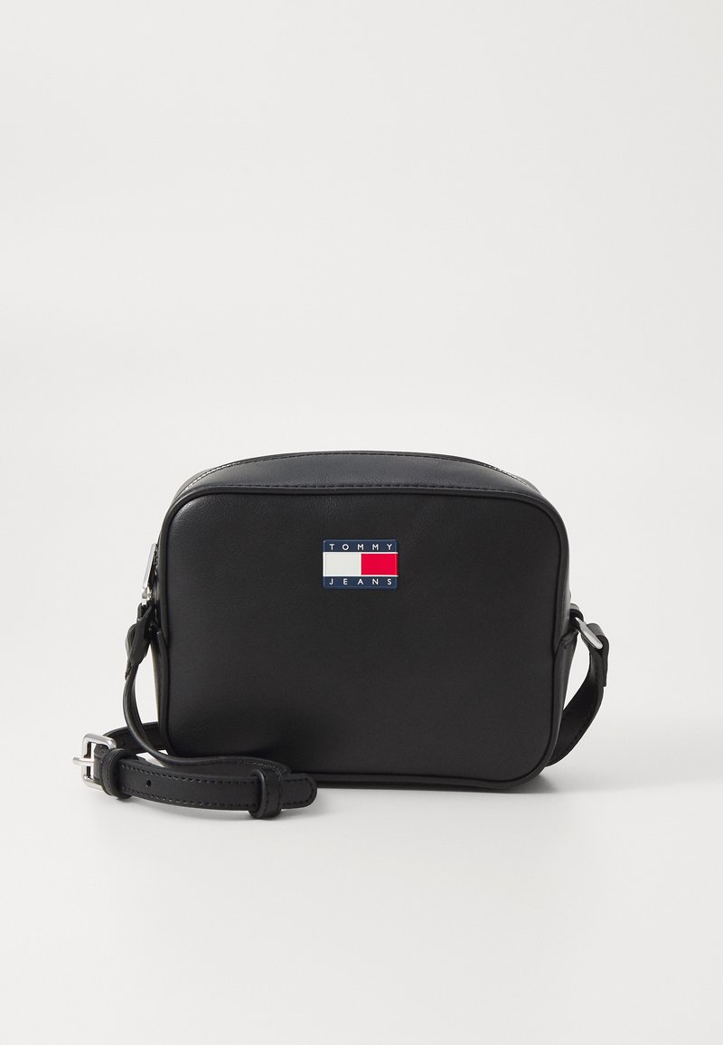 Bolsa de ombro em couro preto com formato retangular, apresentando um logotipo na parte da frente em vermelho, branco e azul. Correia ajustável incluída.