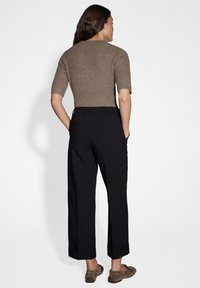 Brown ribbed short-sleeve top paired with black wide-leg trousers featuring an elastic waistband and rolled cuffs. Brown slip-on shoes.