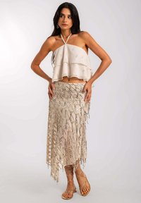 Top court à bretelles superposé beige ; jupe assortie mi-longue avec des détails en sequins délicats et un ourlet frangé. Des sandales à lanières complètent le look.