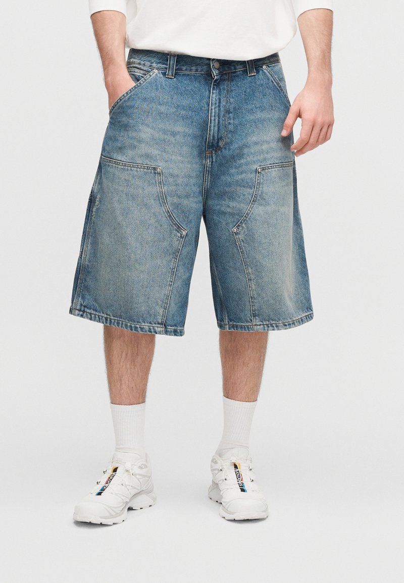 Lyseblå denimshorts med løs pasform, med store forlommer og rå kant. Kombineret med hvide sneakers og sokker.