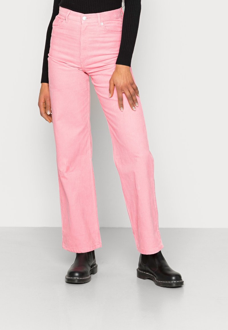 Rosa kordflodda utsvängda byxor med kontrasterande svarta sömmar, hög midja, fem fickor och en texturerad ribbad yta, matchat med svarta stövlar.