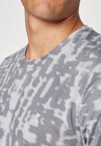 Grå t-skjorte med kort erme og et abstrakt mønster, laget av mykt stoff. Har en liten hvit Under Armour-logo på brystet.