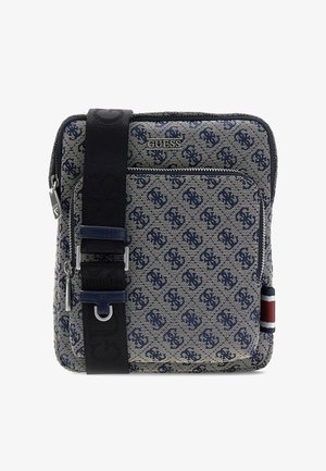 Sac bandoulière carré en tissu à motifs bleus, poche zippée devant, logo Guess, large bandoulière noire et détail de bande latérale rouge-blanc-bleu.
