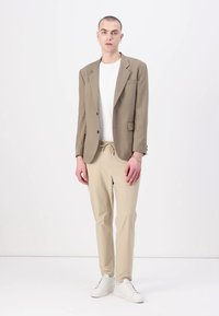 Beige tailored blazer over a white t-shirt, paired with light tan pants and white sneakers. Smooth fabric and structured design.