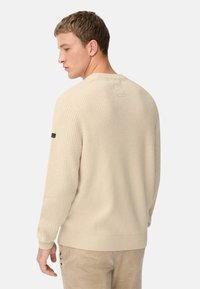 Helles beige, geripptes Sweater mit langen Ärmeln, rundem Ausschnitt und subtilen strukturierten Details auf dem Rücken. Etikett am linken Ärmel.