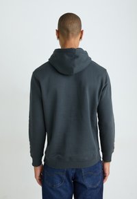 Donkergrijze hoodie met een achteraanzicht, voorzien van een trekkoordcapuchon, geribde manchetten en zoom, gedragen met blauwe jeans. Soepele stoftextuur.