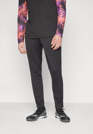 Czarne sportowe spodnie o dopasowanym kroju, wykonane z lekkiego materiału. Do tego dobrała wielokolorowy top z długim rękawem, posiadający wyrazisty, abstrakcyjny wzór.