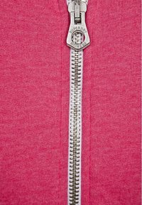Felpa con zip rosa caratterizzata da una zip metallica argento con un tirazip personalizzato, tessuto testurizzato e cuciture accurate lungo i bordi.